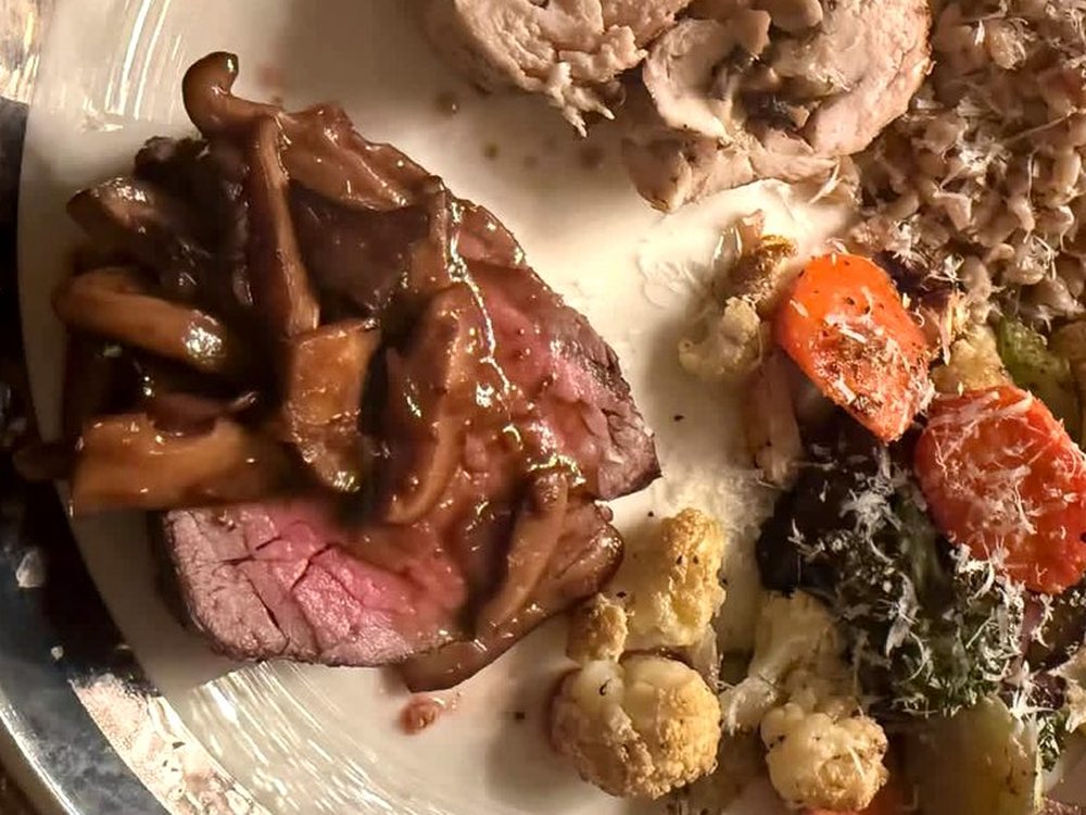 Sliced beef tenderloin with mushroom sauce beside colorful roasted vegetables